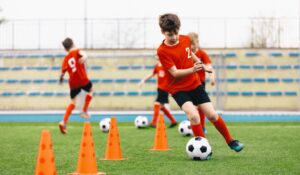 A group of youth soccer players in red uniforms warm up and do drills with cones and soccer balls on a soccer field 