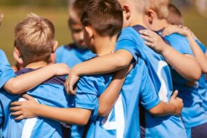 A group of young soccer players in blue uniforms put their arms around each other, learning social skills 