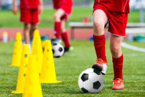 Youth soccer players wearing red uniforms perform soccer practice warm-up drills around yellow cones 