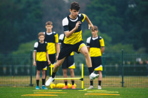 A youth soccer player performs plyometric exercises while his teammates line up behind him on the soccer field  