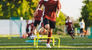 A youth soccer player jumps over a series of hurdles on a field, one of many common plyometric exercises for soccer