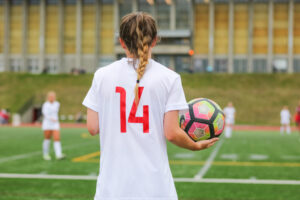 A young female soccer player holds a soccer ball and wonders how to play college soccer